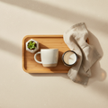 A styled flat lay of everyday home goods including a ceramic mug, plant, candle, linen towel, and wooden tray